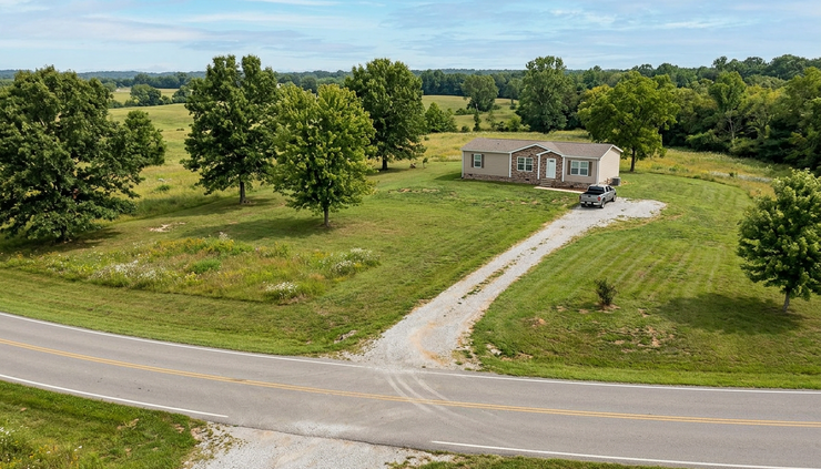 High-angle view of a manufactured home lot with trees and open land.