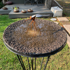 Upcycled satellite dish used as a shallow bird bath. Surface has small stones adhered with resin.