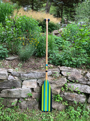 Canoe paddle painted with striped pattern in shades of blue, and green