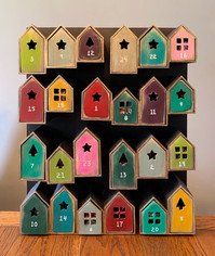 Wood advent calendar with small houses and drawers that hold the Christmas treat. Painted in bright colours with black background.