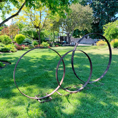 Garden art made with 3 different sized wagon wheel rims welded to metal ladder. 8 feet long