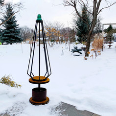 Scrap metal garden sculpture in the form of a pyramidal tree. Made with inverted planter, tractor hub and turquoise glass insulator