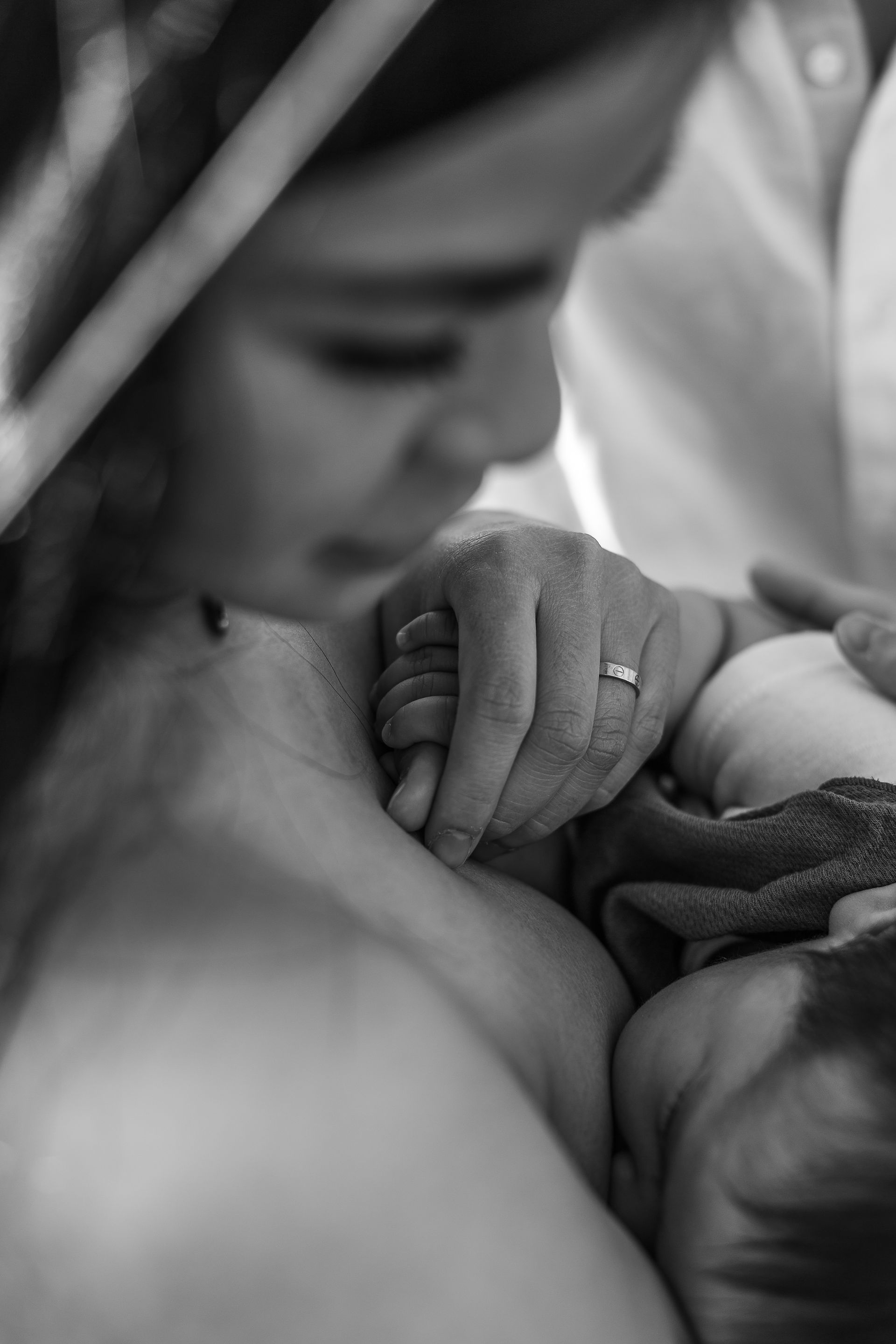 A mother holds her baby's hand as he breastfeeds at a Brisbane family photoshoot