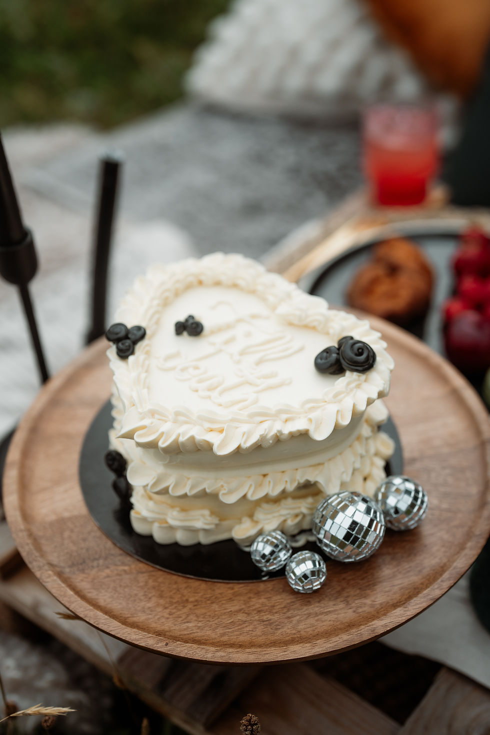 wedding cake saying "till death" sits on stand with tiny disco balls during wedding picnic.