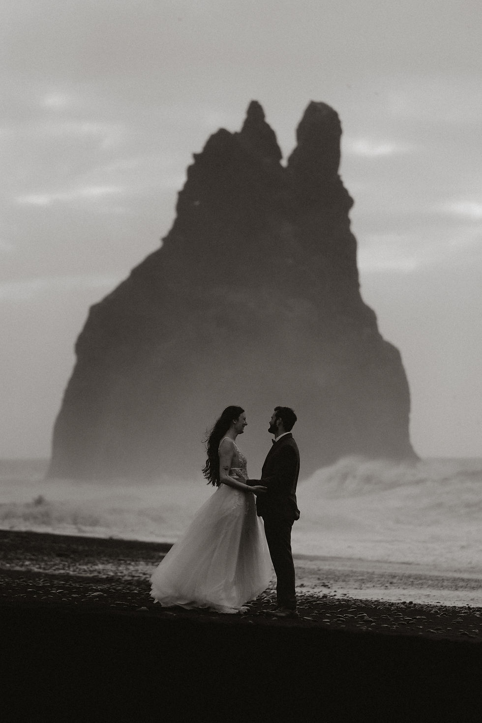 bride and groomo stand on black sand beach in iceland.