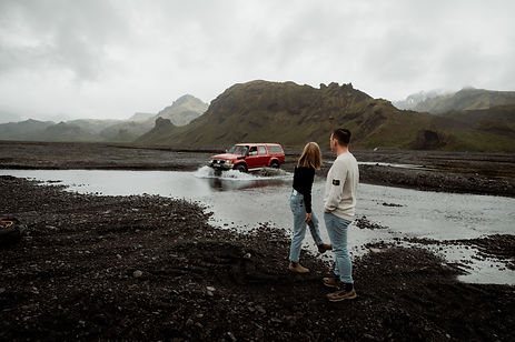 iceland wedding photographer snaps a photo of an engaged couple standing in front of a car going through a river.