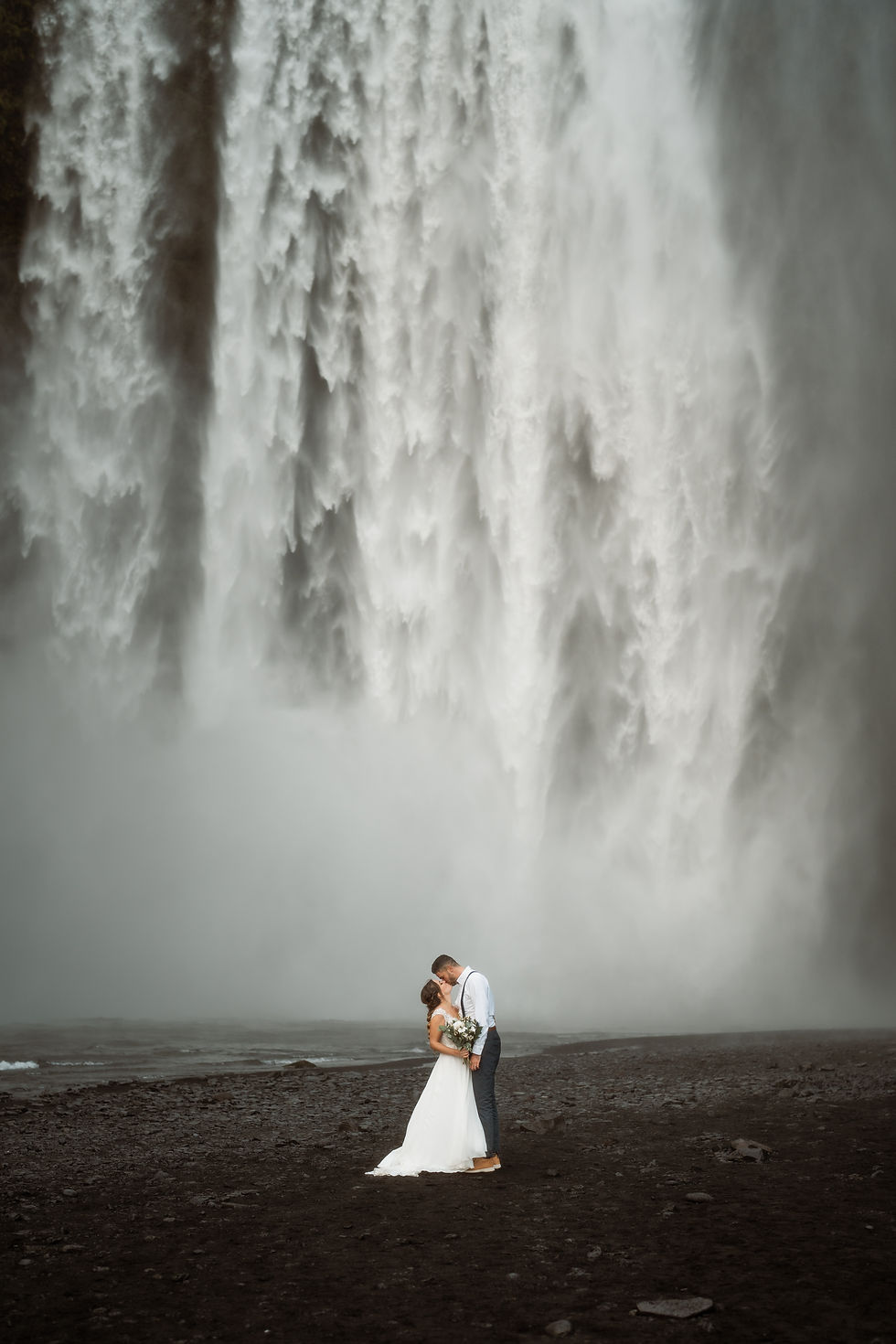 bride and groom kiss in front of waterfall in iceland.