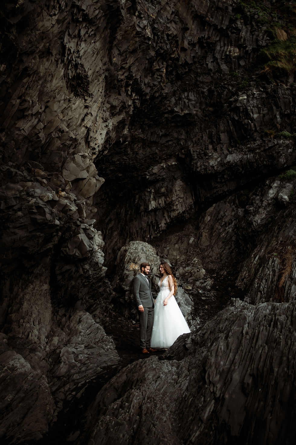 bride and groom stand on rock formations in iceland during honeymoon.