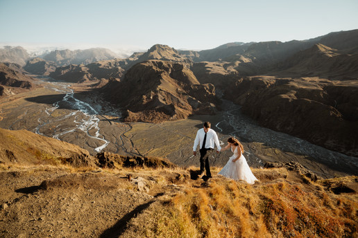 bride and groom hold hands and walk up a hill at one of the best place to elope in iceland