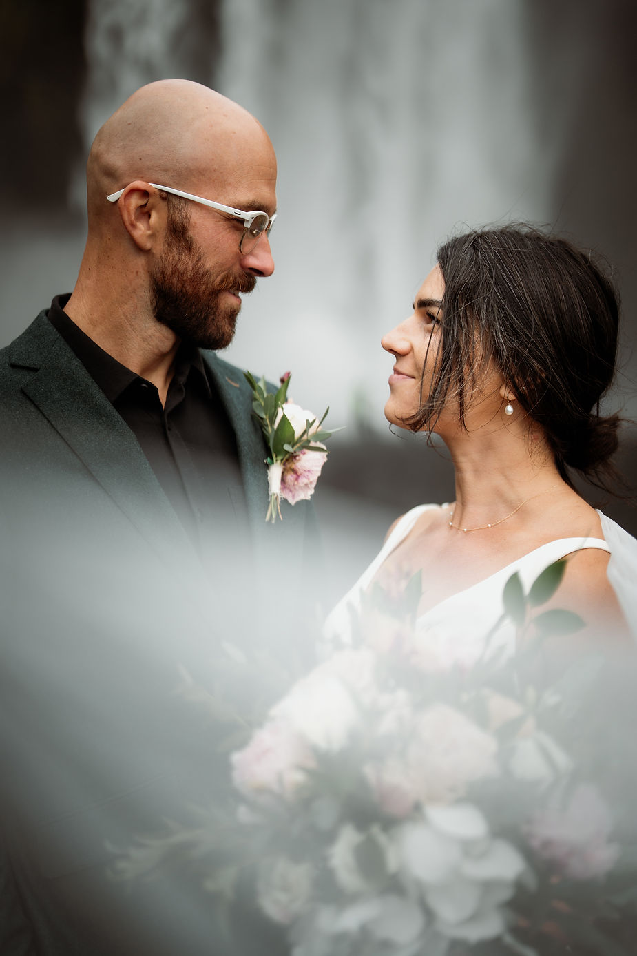 bride and groom look and smile at each other with iceland waterfall in the background.