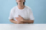 Person in a white shirt holds stomach with both hands, sitting at a white table.