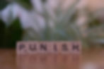 Scrabble tiles spell "PUNISH" on a wooden surface.