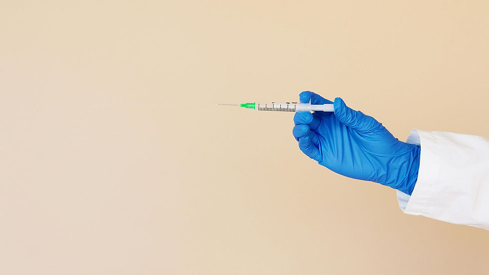A hand in a blue glove holds a syringe with a green tip against a beige background.