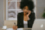 Woman in an office, talking on phone, writing notes. Background features abstract wall art.