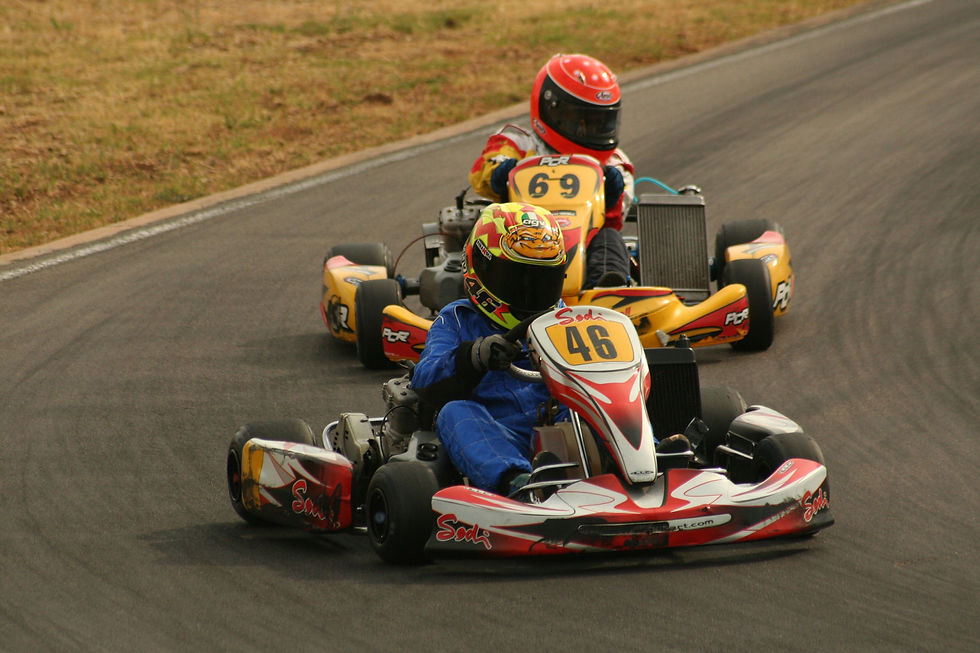 Two go-karts race on a track, blue-suited driver in red-and-white kart 46 leading a yellow kart 69.