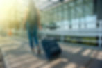 A girl walking towards an airport with a backpack and suitcase dragging behind her