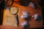 Crumpled papers, handwritten letter with magnifying glass, pen on wooden desk. Warm light creates a thoughtful, creative mood.