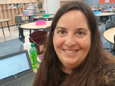 Teacher Elizabeth at a desk in a classroom in front of a computer.