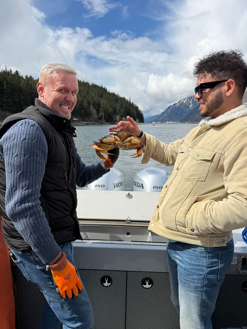 Two men holding a large crab on a boat with mountains.