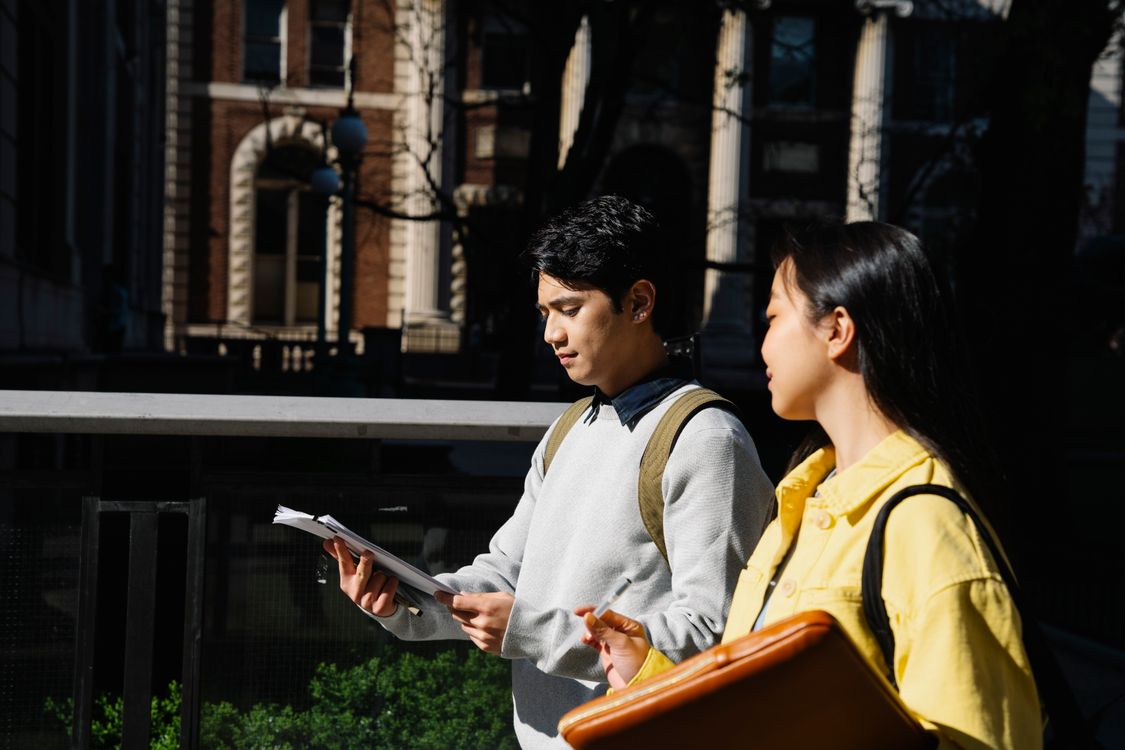 Two university students walking on campus while discussing notes, illustrating field observation and survey research