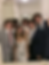 Five teens in formal outfits take a mirror selfie in a white bathroom, smiling and laughing, with phones and suits visible.
