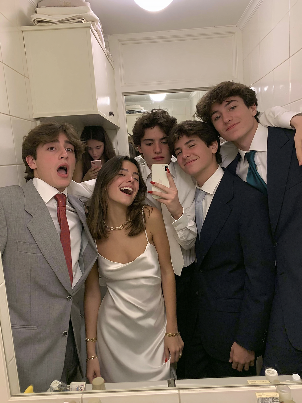 Five teens in formal outfits take a mirror selfie in a white bathroom, smiling and laughing, with phones and suits visible.