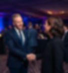 Magician Ryan Joyce in a blue sequin performance suit shaking hands with an event organizer at a high-end corporate gala.