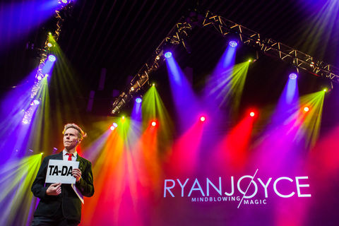 Magician Ryan Joyce standing on stage with bright vibrant lights behind him at a massive corporate event in Vancouver