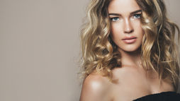 Woman with wavy blonde healthy hair wearing a black off-shoulder top, showing shine and strength that reflect tips on how to get healthy hair.