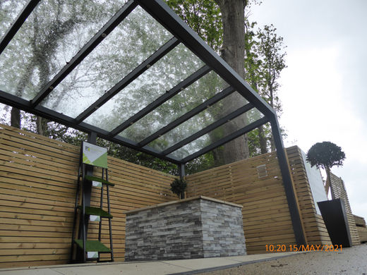 Anthracite grey glass roof pergola with timber wall and grey stone fireplace.