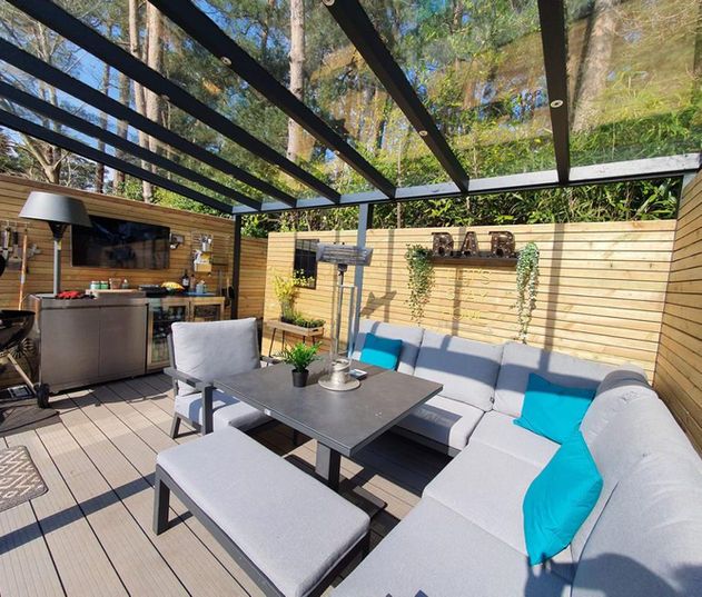 Anthracite grey aluminium pergola with glass roof, timber cladding, garden sofas and grill. Installed in Camberley, Surrey.
