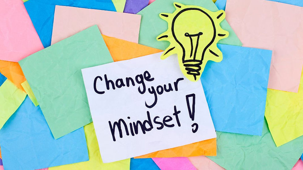 Note with "Change your mindset!" on colorful paper background. A yellow paper lightbulb symbolizes ideas and positivity.