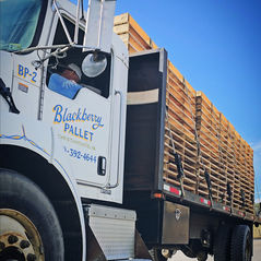 Truck labeled "Blackberry Pallet" carries wooden pallets under a clear blue sky. Driver visible in cab. Text: Christiansburg, VA.