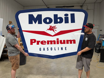 Two men holding large Mobil Premium Gasoline sign in custom signage solutions.