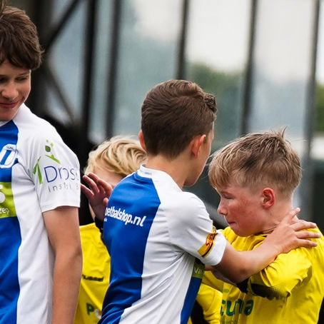Jeugdspeler in geel shirt tussen grotere tegenstanders tijdens een voetbalwedstrijd