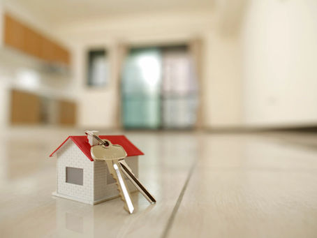 Mini house with red roof and metal keys on a tiled floor. Blurred modern kitchen in the background suggests a new home concept.