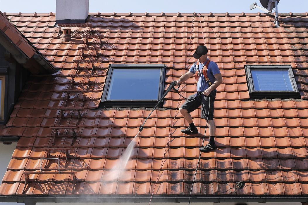 Professional worker pressure washing terracotta roof tiles near skylights for roof cleaning work