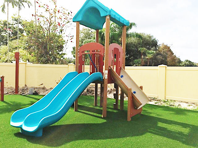 green, red, and tan climber with roof, slide, ramp climber, and block climber on grass turf at school daycare playground