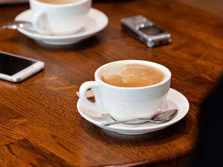 A smartphone and portable voice recorder beside coffee cups on a wooden table