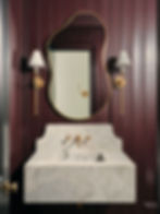 Residential interior design - maroon color-drenched powder bath with marble sink, wavy mirror, and floor to ceiling paneling.