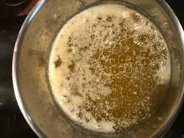 Liquide doré et clair de ghee en formation dans une casserole, après la disparition de la mousse, avec une cuillère en bois