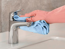 Cleaning limescale from a chrome tap using a cloth and gloves in a bathroom sink
