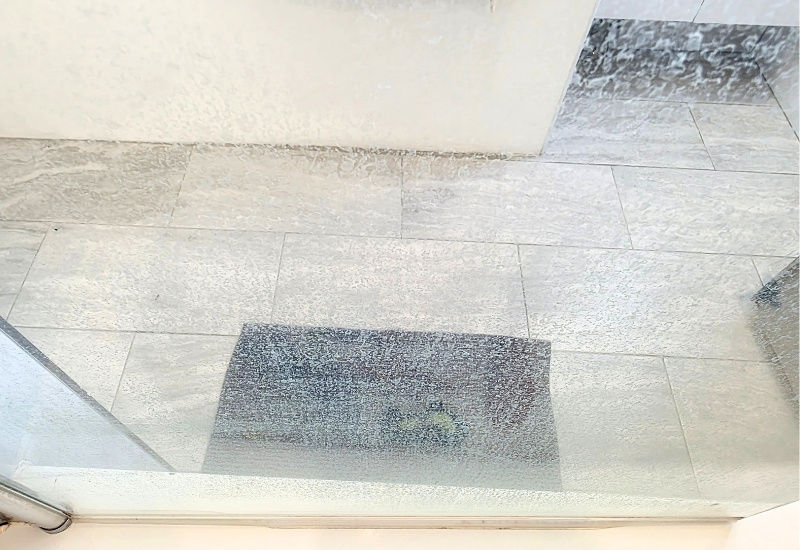 Heavy limescale buildup on a shower screen showing cloudy glass caused by hard water deposits