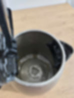 Open electric kettle with limescale buildup inside, placed on a light wooden surface.