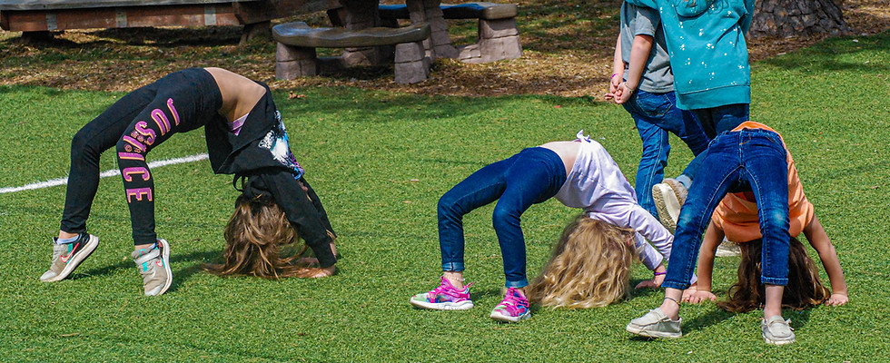 Three girls playing outside in the grass, all three are doing backbends