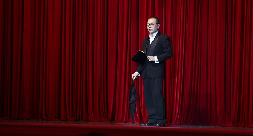 Kemin Zhang Magician MC in front of red curtain with an umbrella and holding a change bag hosting Westlake International Magic Convention in Hangzhou