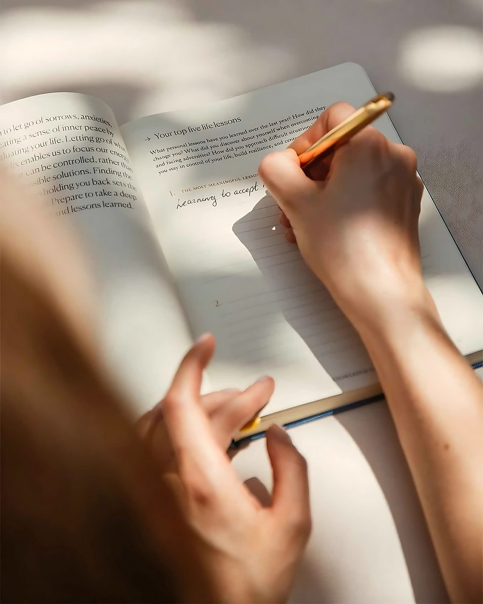 Writing a reflection in a journal on a table, with soft sunlight casting shadows.