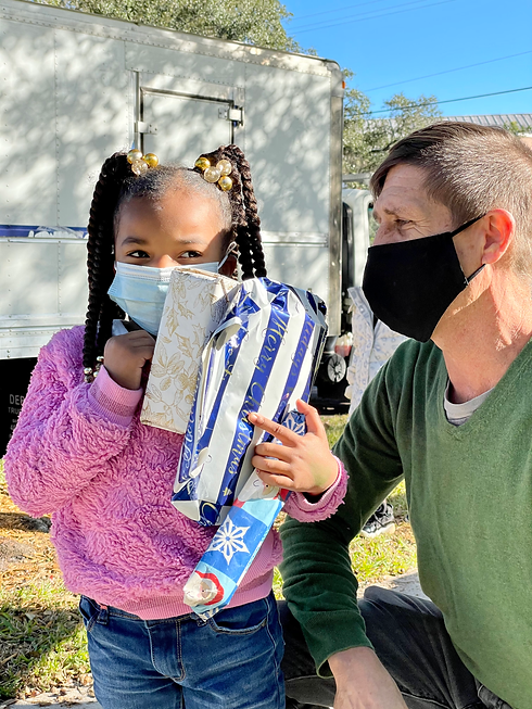 Picnic Project co-founder Ryan Bozeman sharing Christmas gifts with small girl in braids.