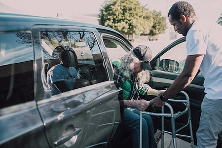 Young adult helping an elderly person out of a car.