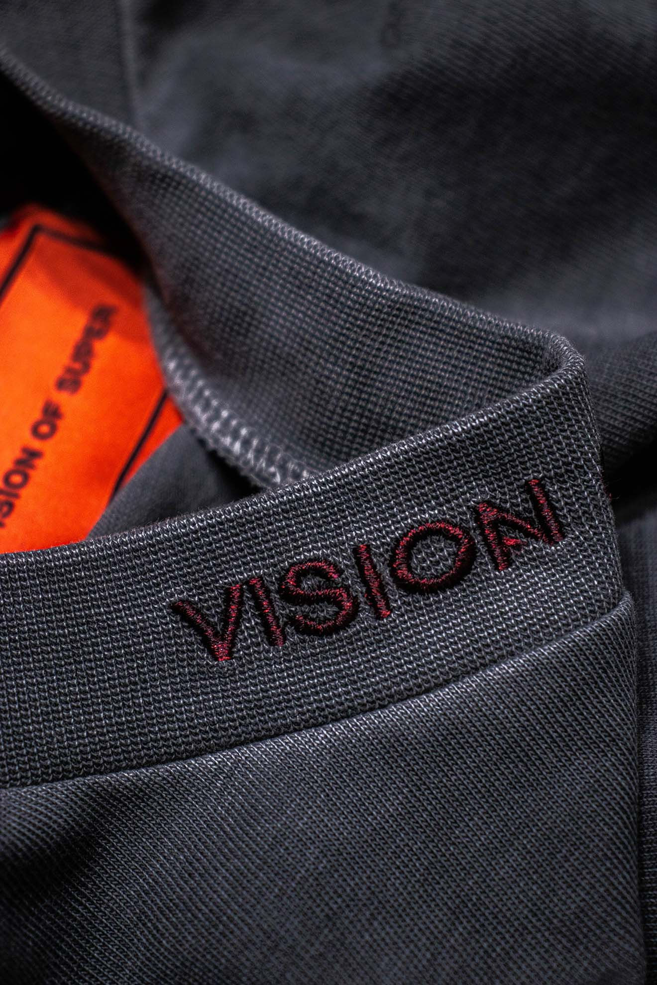 Áo tối màu với chữ thêu đỏ, nhãn VISION OF SUPER.